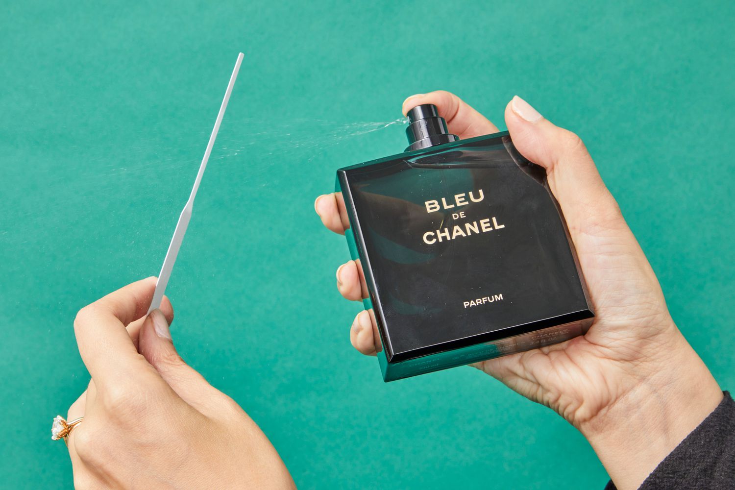 A person spraying Chanel Bleu de Chanel Parfum onto a tester in front of a green background